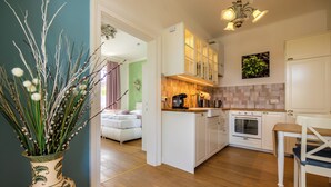 A modern kitchen with white cabinetry, a built-in oven, and a dining area with a wooden table and chairs. - Albizia-Apartments (Baden)