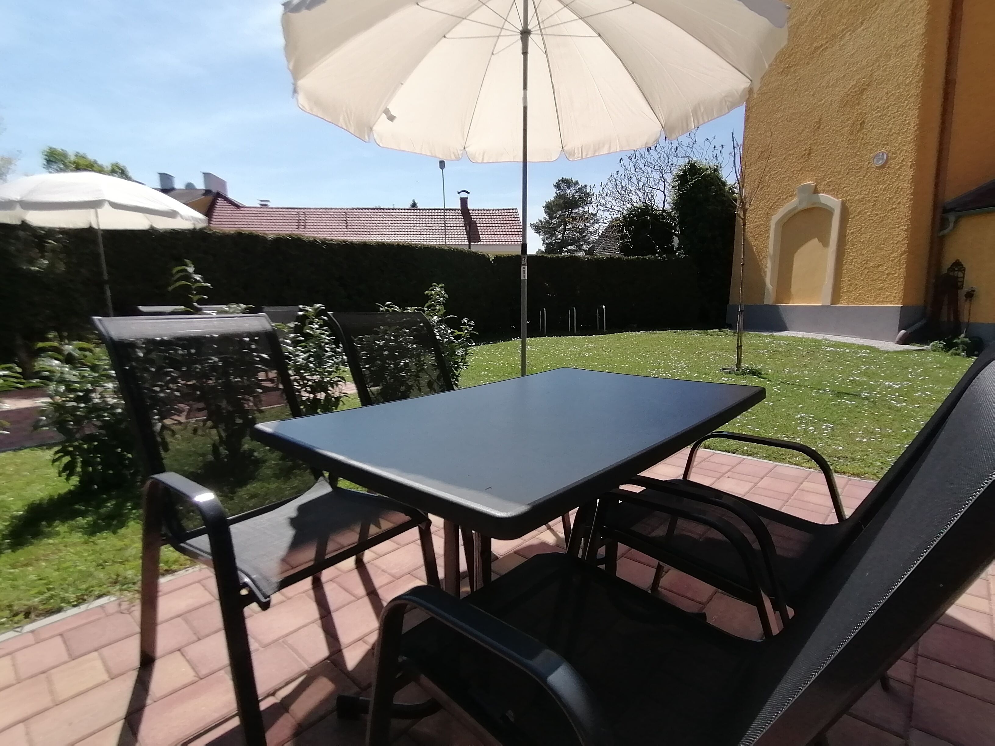 Un patio con una mesa, sillas, una sombrilla y un seto al fondo.