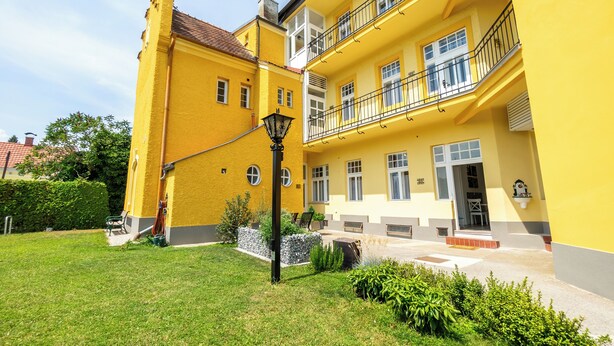 A yellow building with a balcony, a lawn, and a street lamp. - Albizia-Apartments (Baden)