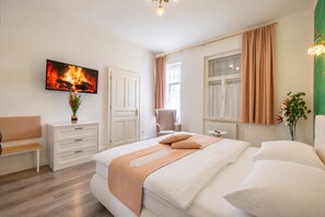 A bedroom with a bed, a chair, a dresser, a TV, and a window with curtains.