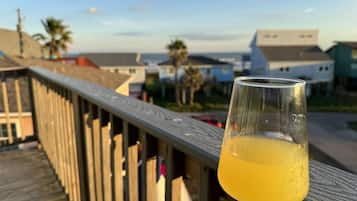 A glass of orange juice on a wooden deck with a view of houses and palm trees in the background.