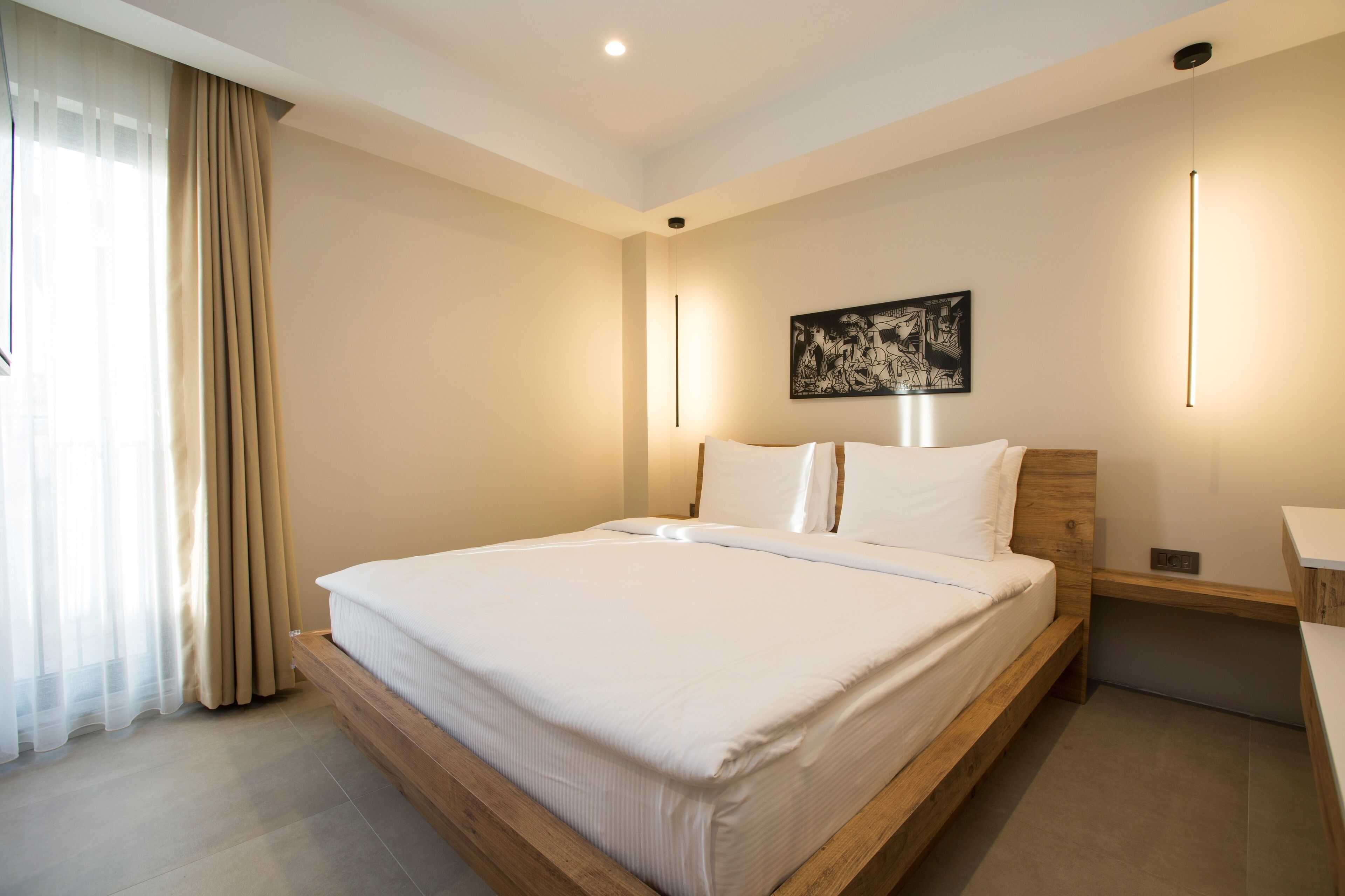 A modern hotel room with a large bed, wooden headboard, and a painting on the wall.