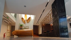 A modern lobby with a central seating area, a reception desk, and a staircase leading to upper floors. - Nilus Urla (Urla)