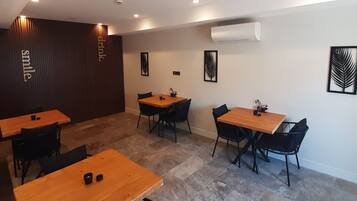 A modern dining area with wooden tables and black chairs, recessed ceiling lighting, and decorative wall art.