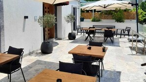 An outdoor café with wooden tables and chairs, large umbrellas, and potted plants. - Nilus Urla (Urla)