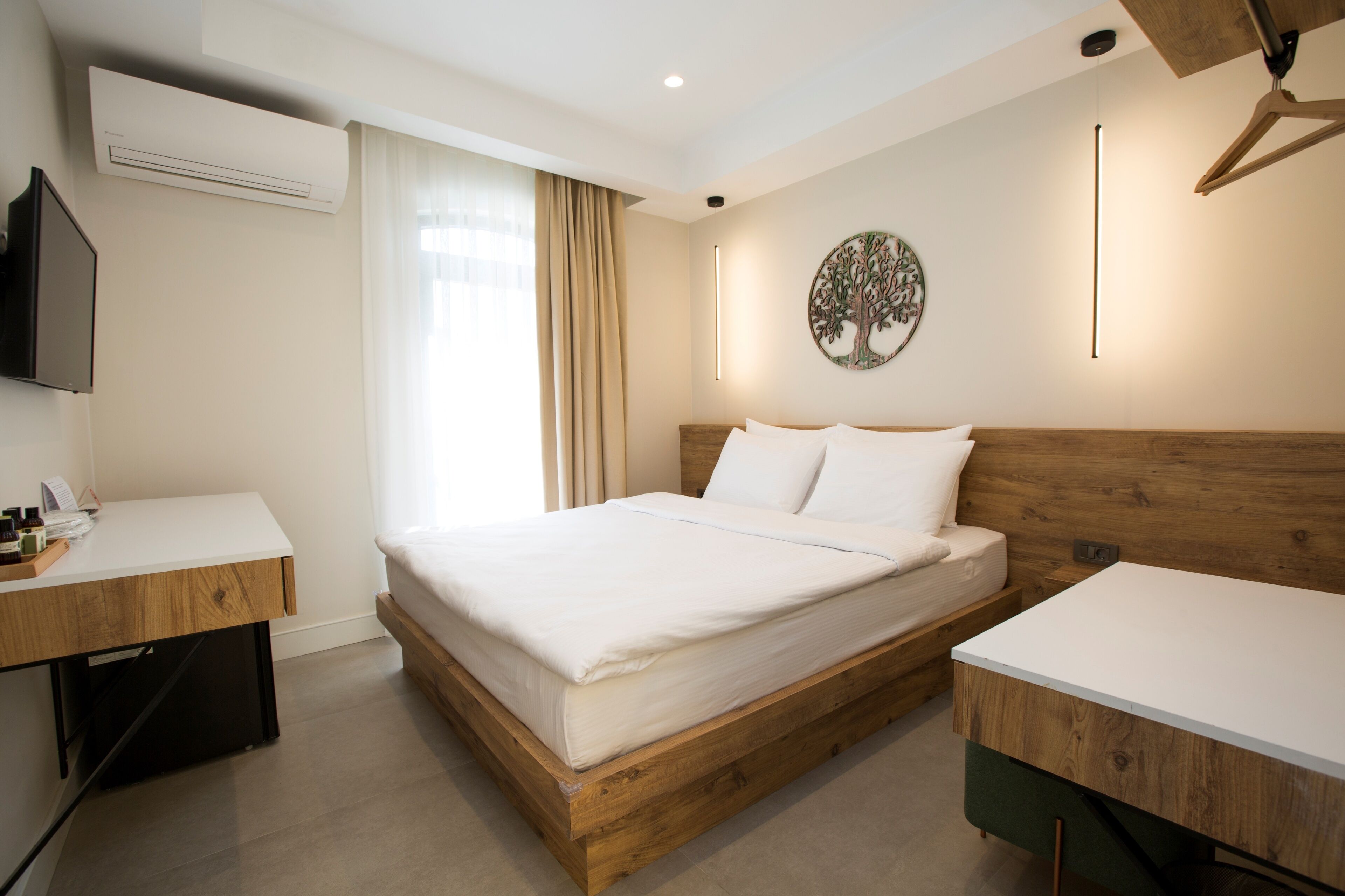 A hotel room with a wooden bed frame, a white desk, a flat-screen TV, and a wall-mounted artwork.