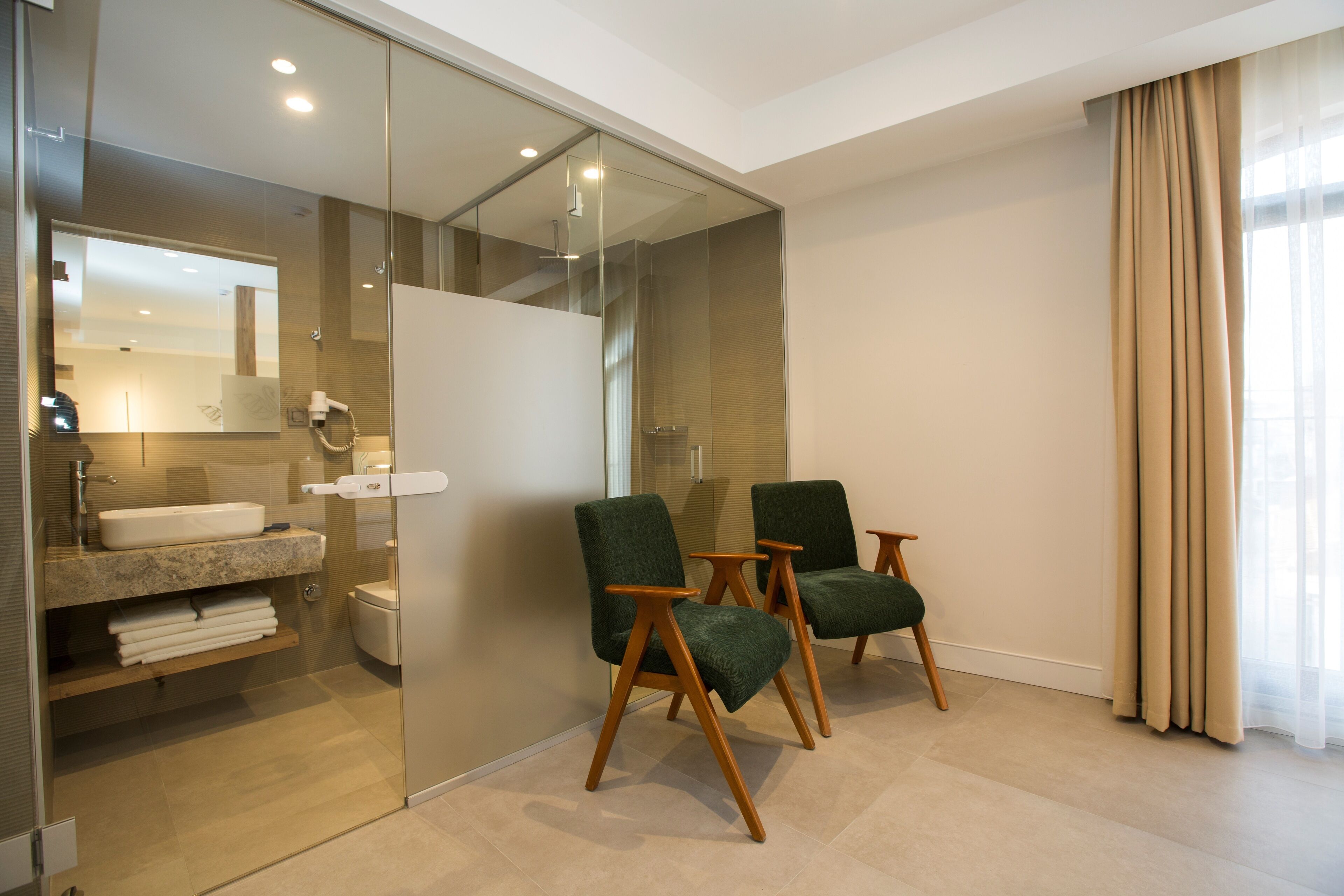 Une salle de bain moderne avec une cloison en verre, un lavabo et deux chaises vertes.