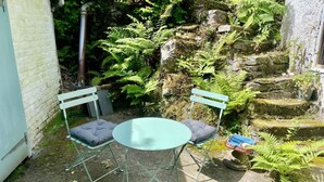A small outdoor seating area with two chairs and a table, surrounded by greenery and stone steps.