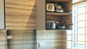 A kitchen with a gas stove, oven, and a shelf above the sink holding pots and pans.