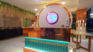 A reception area with a circular sign reading "KITCHEN MINISTRY," a plant, and a QR code for a mobile app. - HOTEL THE GRAND TARA (Indore)