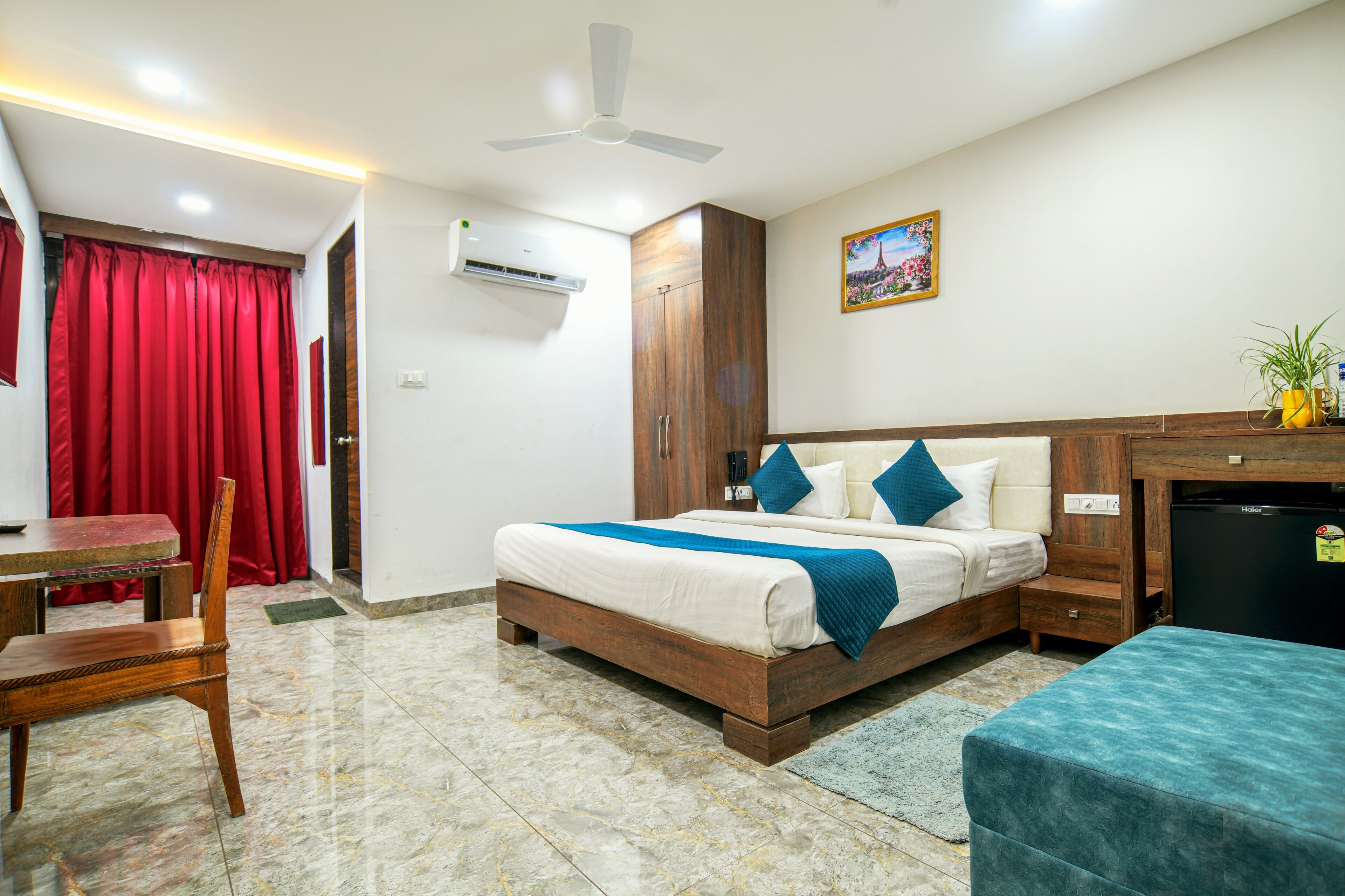 A hotel room with a bed, a desk, a chair, a ceiling fan, and a wall-mounted air conditioner.