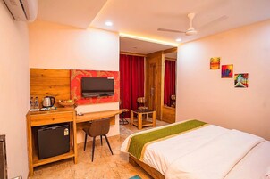 Una habitación de hotel con cama, escritorio, televisor y un refrigerador pequeño.