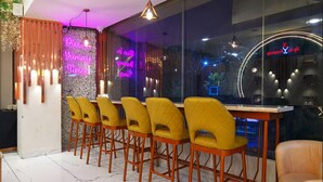 A modern bar area with a row of yellow chairs, a neon sign, and a glass wall with a view of the city. - HOTEL THE GRAND TARA (Indore)