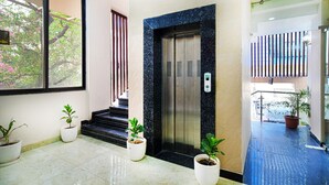 An elevator with a marble surround, potted plants, and a view of a building outside. - HOTEL THE GRAND TARA (Indore)