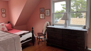 Une chambre à coucher comprenant un lit, une commode, une chaise et une fenêtre donnant sur l’extérieur.