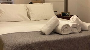 Una camera d'albergo con un letto rifatto, lenzuola bianche e asciugamani arrotolati sul letto.