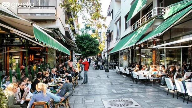 Un caffè all'aperto con tavoli e sedie, circondato da edifici con tende verdi.
