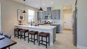 Una cocina moderna con gabinetes grises, una isla central con taburetes, un microondas y un refrigerador.