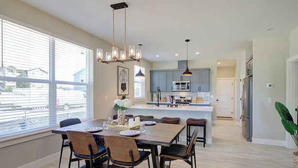 Una cocina moderna con una isla central, ventanas amplias y un comedor con mesa y sillas de madera.