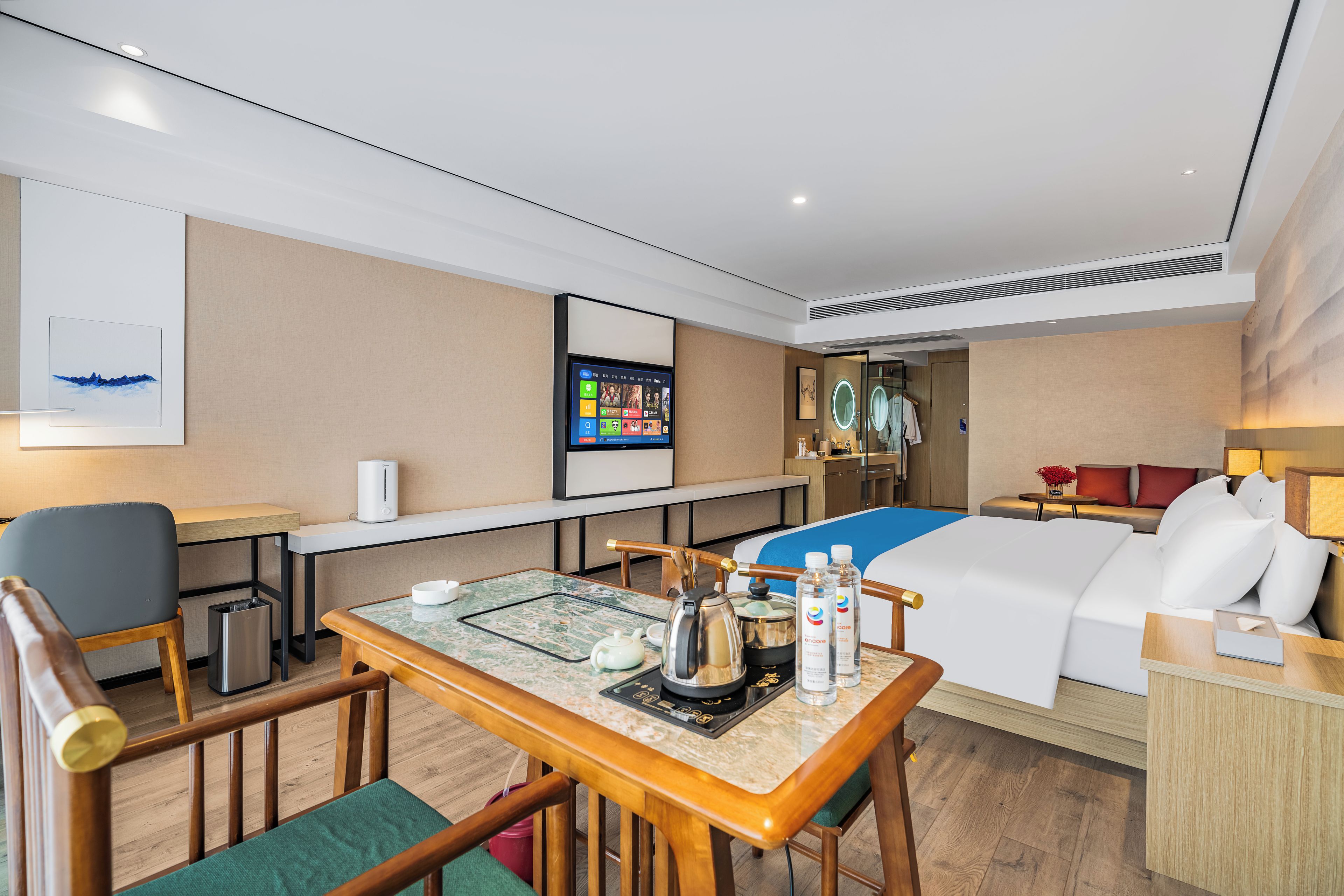 Ein Hotelzimmer mit einem Bett, einem Schreibtisch, einem Sessel, einem Tisch mit Teekanne und einem Fernseher.