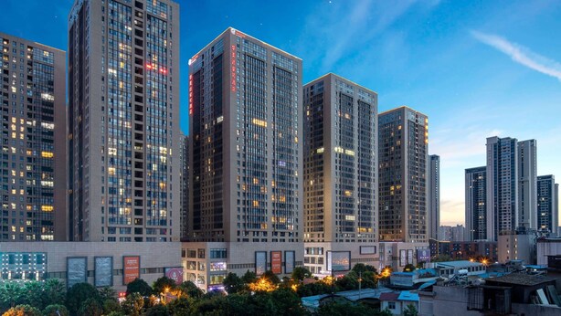 A high-rise building complex with multiple floors, large windows, and illuminated signs. - Ramada Encore by Wyndham Kunming Guandu (Kunming)