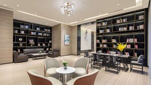 A modern library with multiple bookshelves, a seating area with chairs and a table, and a decorative ceiling light. - Ramada Encore by Wyndham Kunming Guandu (Kunming)