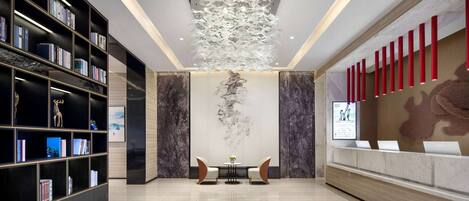 A modern lobby with a black bookshelf, a round table with chairs, and a unique ceiling light fixture.
