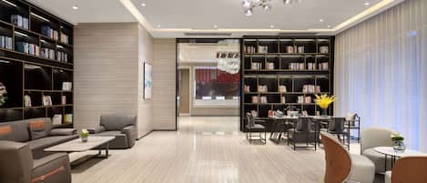 A modern living room with a sofa set, a coffee table, and a dining area with chairs and a table. There are two large bookshelves filled with books and decorative items.