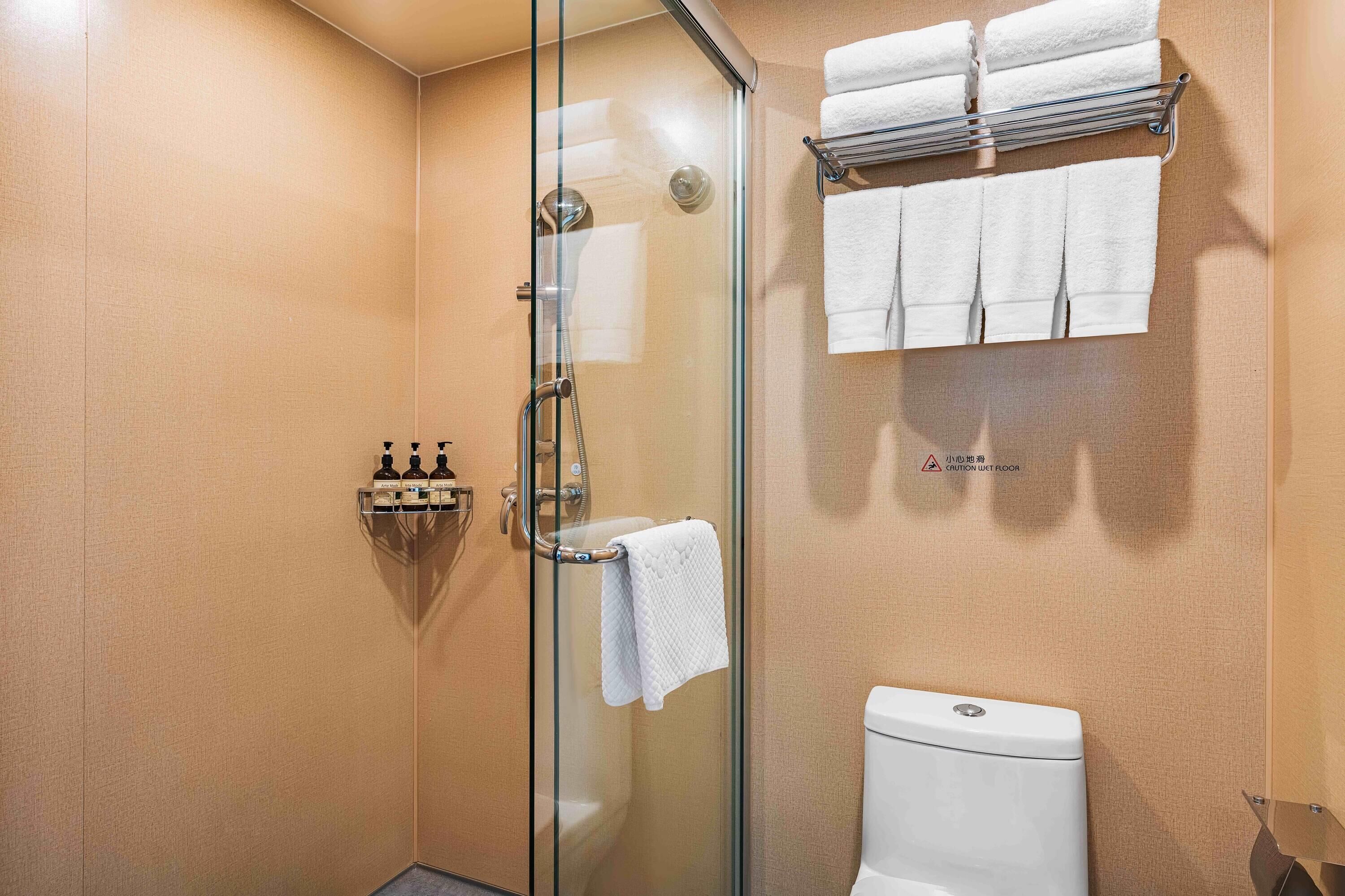 A bathroom with a glass-enclosed shower, a toilet, and a towel rack with multiple towels.