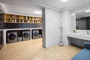 Un moderno lavadero con tres lavadoras apiladas, un estante con libros y objetos decorativos, y un espejo grande sobre el lavabo.