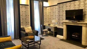 A modern living room with a sofa, armchair, coffee table, fireplace, television, and a desk with a lamp. - 1 Bed Luxury Flat, Ground Floor, Sky TV, Air Con (Greater London)