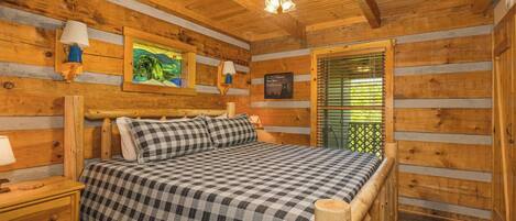Un dormitorio tipo cabaña de troncos con una cama, mesitas de noche, un ventilador de techo y una ventana con persianas.