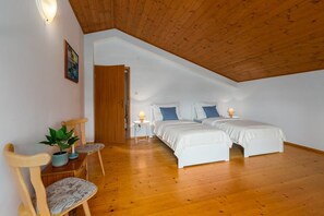 Ein Schlafzimmer mit zwei Betten, Holzboden, Balkendecke, einem kleinen Tisch mit Lampe und einem Sessel mit Pflanze.