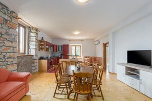 Ein gemütliches Wohnzimmer mit einem Holzesstisch und Stühlen, einem roten Sofa und einem Fernseher auf einem Schrank.