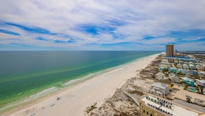 A coastal hotel with a beach view, a parking area, and a tall building in the background. - Phoenix West Ii 1703 3 Bedroom Condo (Orange Beach)