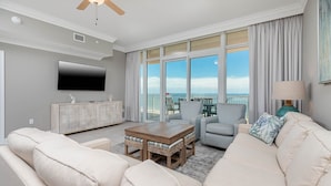 A modern living room with a large TV, comfortable seating, a wooden coffee table, and a view of the ocean. - Phoenix Orange Beach Ii 902 3 Bedroom Condo (Orange Beach)