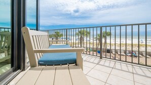 A balcony with a cushioned bench overlooking a beach.