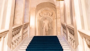A grand staircase with a statue at the top, flanked by ornate balustrades and a chandelier. - Palazzo Roma - The Leading Hotels of the World (Rome)