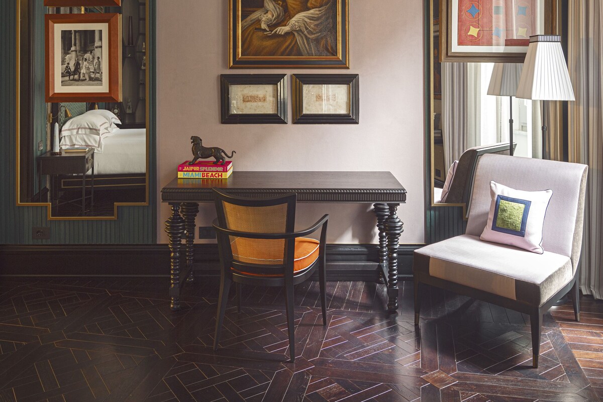 A room with a bed, a table with chairs, a framed portrait, and a mirror.