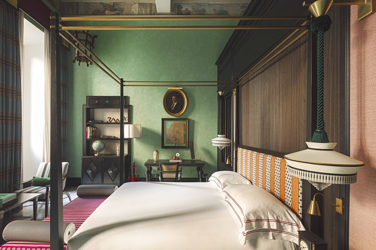 A room with a four-poster bed, a desk with a globe, a chair, a bookshelf, and a wall-mounted lamp.