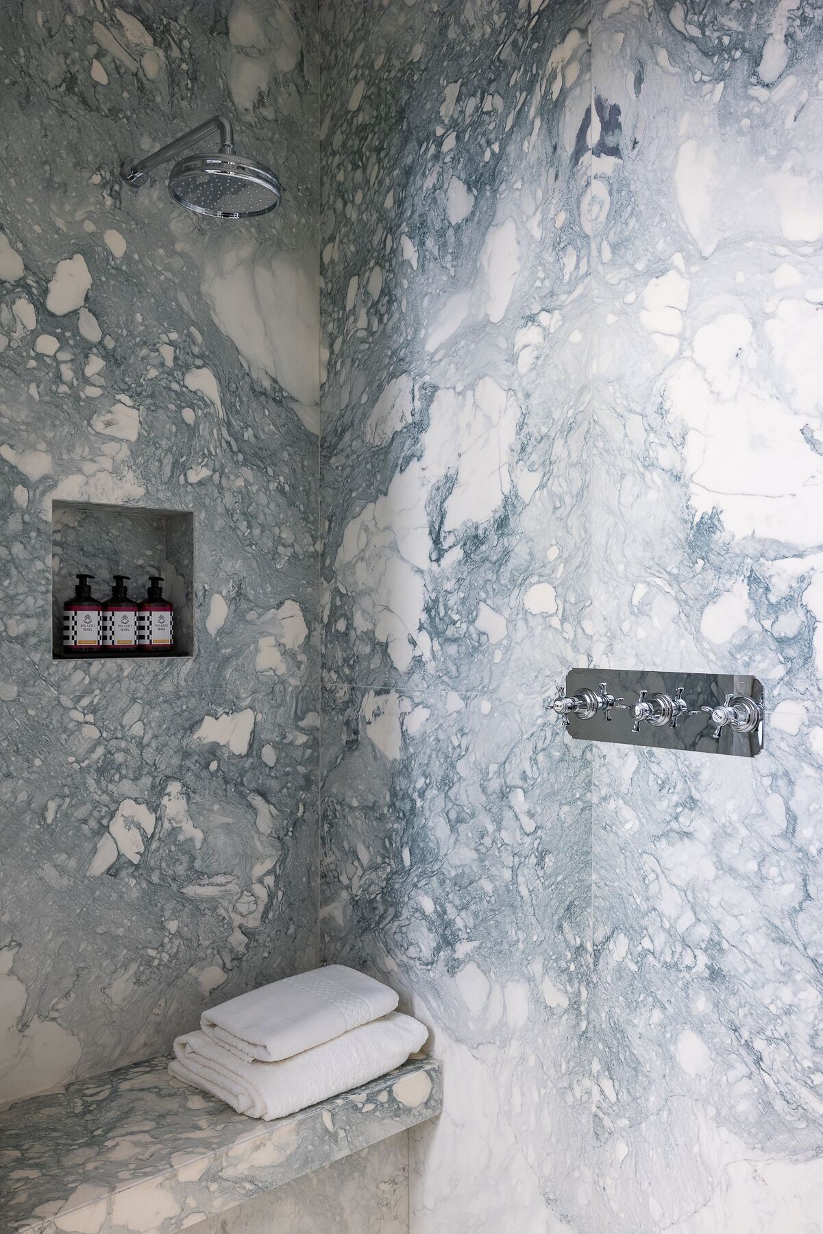 A bathroom with a marble wall, a showerhead, a soap dispenser, and a towel rack.
