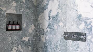 A bathroom with a marble wall, a showerhead, a soap dispenser, and a towel rack.
