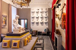 A luxurious room with a large statue, a sofa with striped cushions, a chandelier, and a wall with musical instruments and busts.