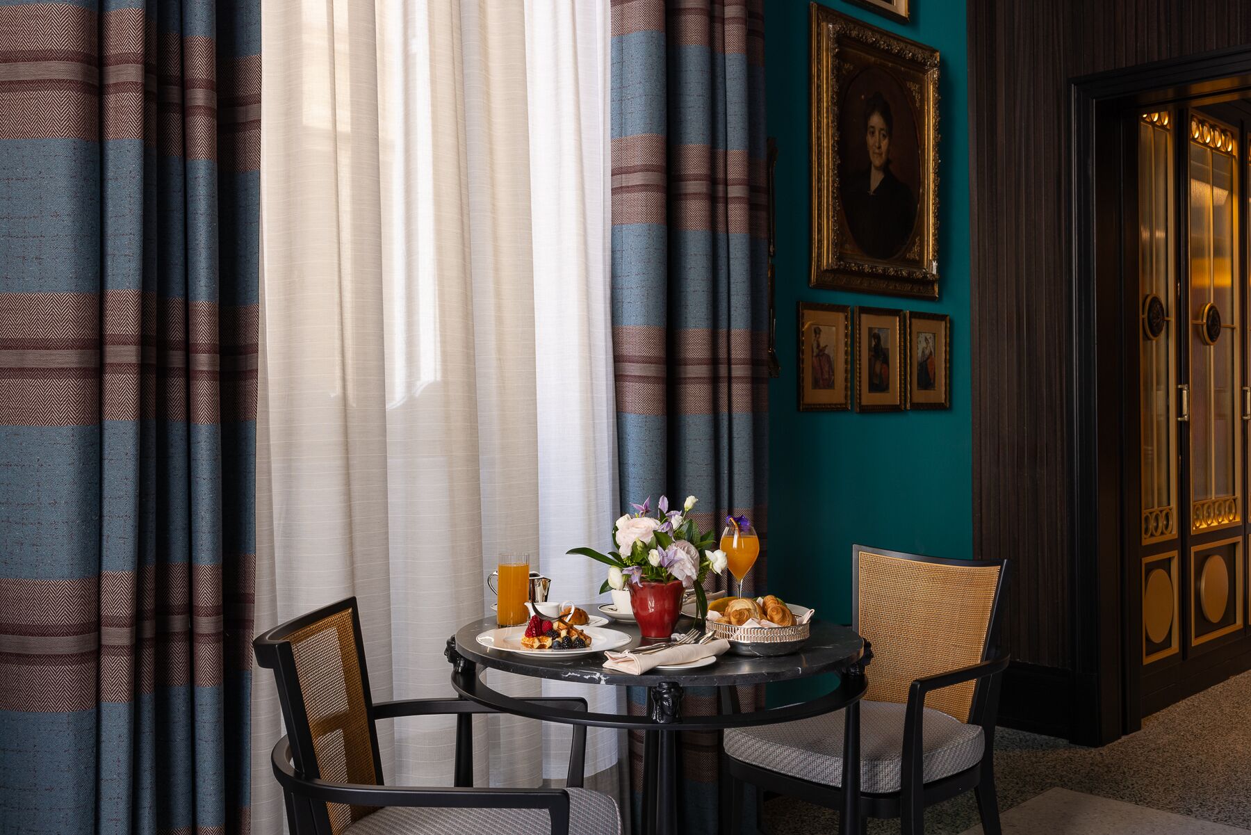 A dining area with a table set for breakfast, featuring croissants, a pitcher, and a vase of flowers.