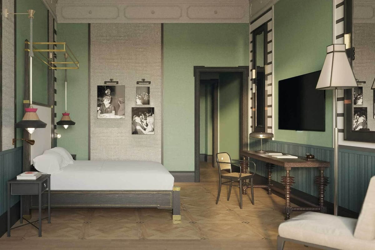 A bedroom with a bed, bedside tables, a desk, and chairs. There is a mirror, a lamp, and framed pictures on the wall.