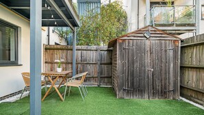 A backyard with artificial grass, a wooden shed, and a table with chairs. - Spacious 2BR with Terrace by King's Cross (London)