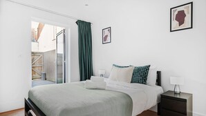 A bedroom with a bed, a nightstand, a window with curtains, and a door leading to a balcony. - Spacious 2BR with Terrace by King's Cross (London)