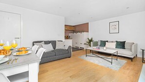 A modern living room with a grey sofa, a coffee table, and a dining area with a white table and chairs. - Spacious 2BR with Terrace by King's Cross (London)