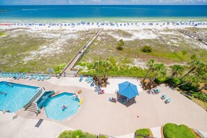 A beach resort with a swimming pool, beach umbrellas, and a boardwalk leading to the beach.