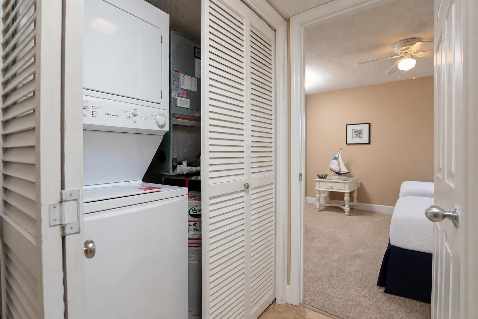 A room with a bed, a bedside table with a decorative item, a ceiling fan, and a door leading to a closet with appliances.